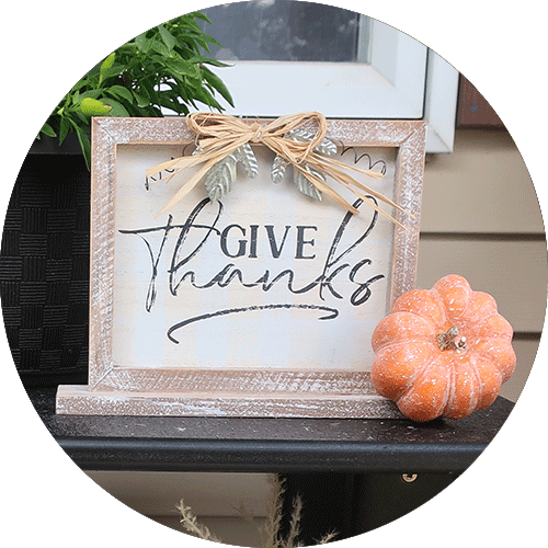 A table top sign that reads Give Thanks, with a small orange pumpkin next to it.